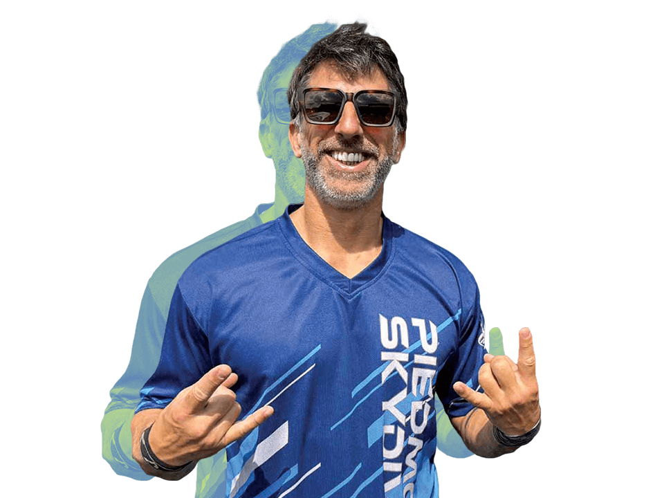 A man wearing sunglasses and a blue sports shirt smiles and makes the "rock on" hand gesture with both hands. A translucent, green-tinted duplicate of his image is visible behind him.